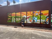 Artist Hannah Legg poses with a seven-panel mural she created in Foley's "Cat Alley Walkway." The alley will be transformed into a public space to allow more connectivity and walkability in Foley's historic downtown. (Photo courtesy Foley Main Street)